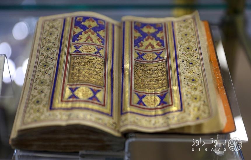 تصویری از یک قرآن کتابت‌شده بر روی پوست که در حفاظی شیشه‌ای داخل موزه قرآن و نفایس حرم امام رضا نگه‌داری می‌شود. 
